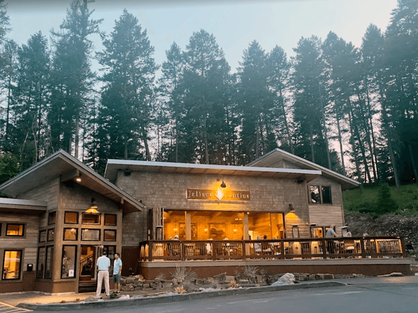 The Jalisco Cantina restaurant at dusk — a timber and shingle building with a lit sign and a full covered patio, backed by tall pines.